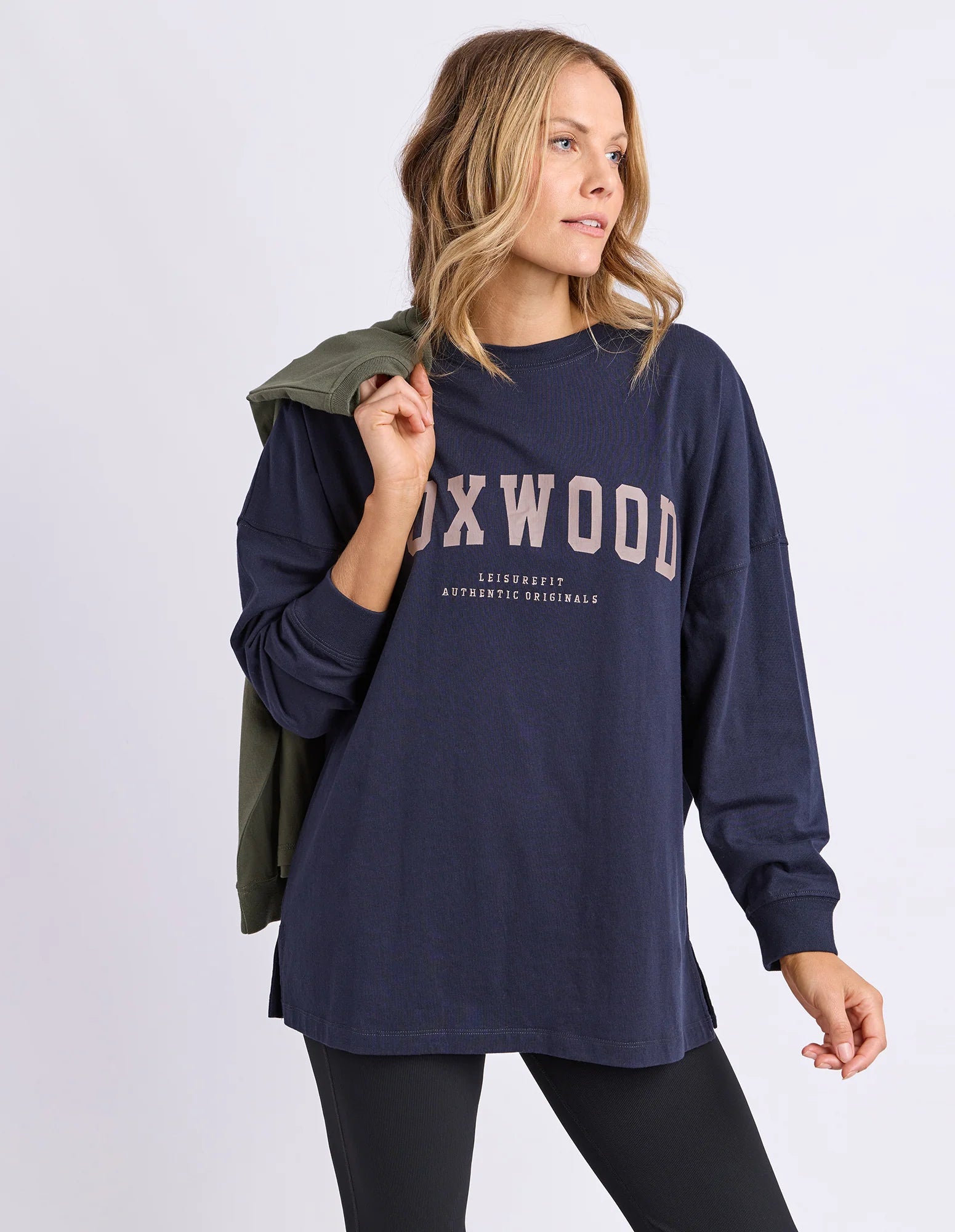 Image of Woman wearing a navy blue long sleev tee with 'FOXWOOD' branding in brown on a light grey background