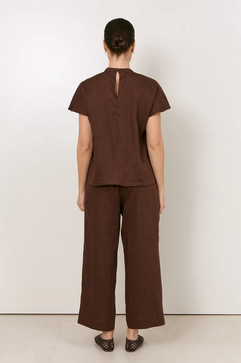 A model viewed from the back wearing a Adorne dark brown linen two-piece set consisting of a short-sleeve top with a keyhole back and matching wide-leg trousers, set against a plain white studio background.