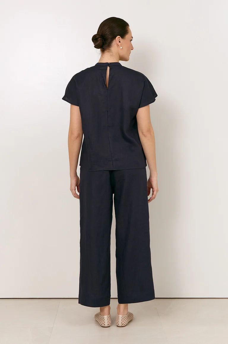 A woman viewed from the back wearing a Adorne dark navy short-sleeve top with a keyhole back cutout and matching wide-leg cropped pants, standing against a plain light wall.