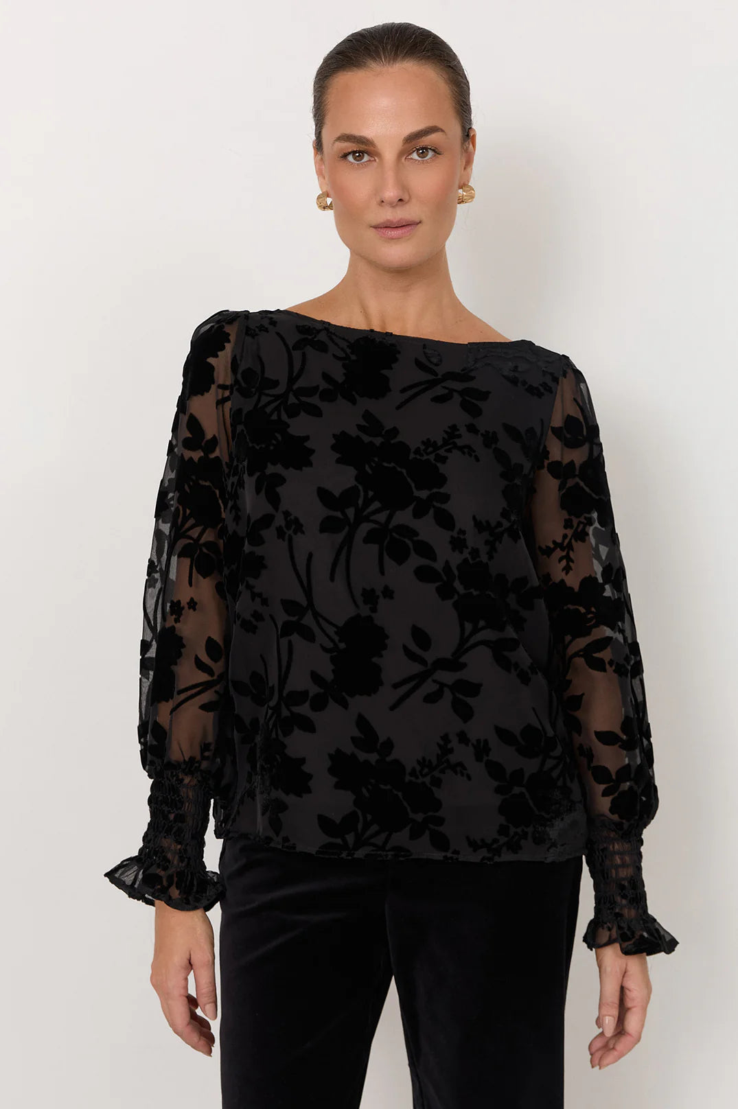 Image of Woman wearing Adorne black shirt featured with flowers paired with black pants on a white background 