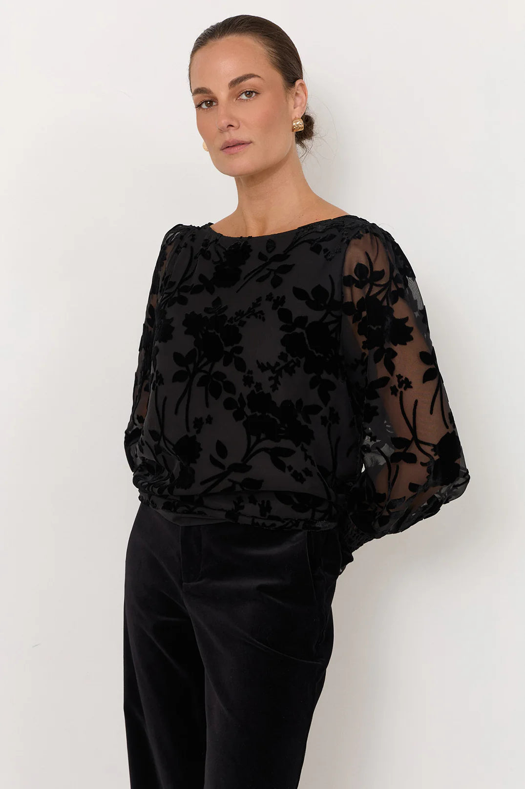 Woman wearing Adorne black shirt pictured with black flowers paired with black pants on a white background 