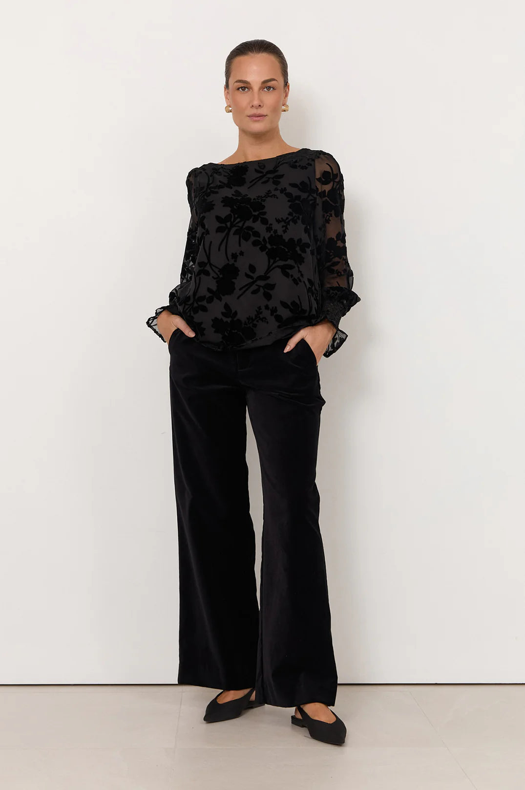 Woman wearing Adorne black shirt pictured with black flowers paired with black pants on a white background 