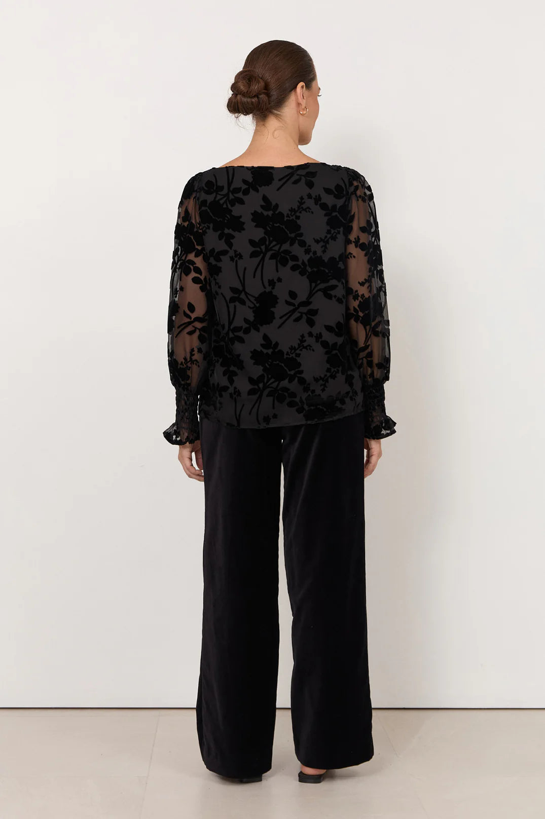 Image of Woman wearing Adorne black shirt pictured with black flowers paired with black pants on a white background 