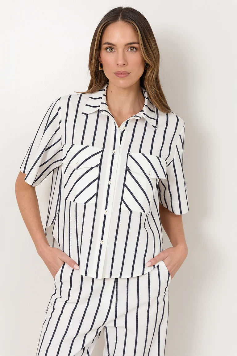 Image of A woman modeling a Adorne matching short-sleeve button-up shirt and striped pants set in white with thin black vertical stripes, posed against a plain off-white studio background.