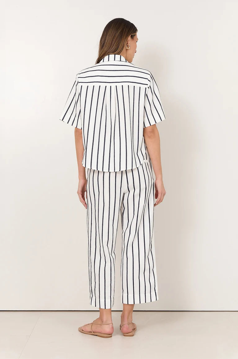 Image of A woman viewed from the back wearing a Adorne matching white two-piece set with thin black vertical stripes, consisting of a short-sleeve button-up shirt and cropped pants, paired with beige flat sandals.