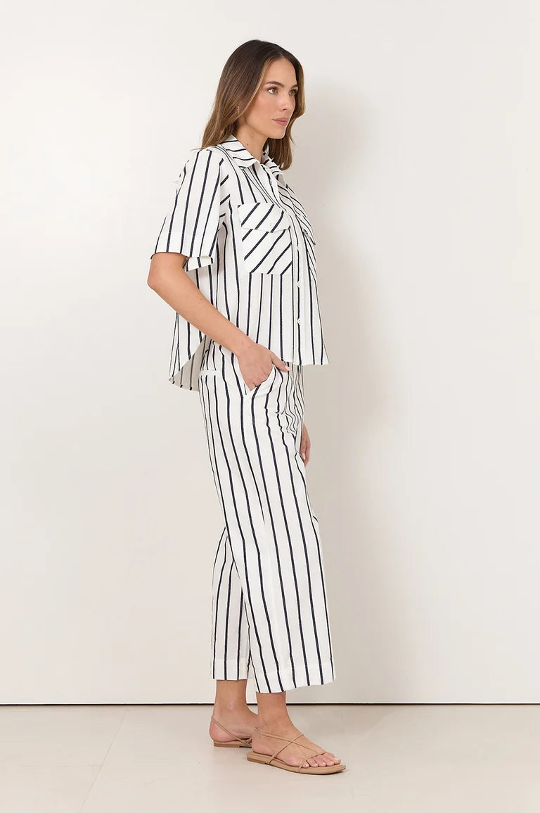 Image of A woman modeling a Adorne matching two-piece set consisting of a short-sleeve button-up shirt and cropped pants, both featuring a black and white vertical stripe pattern. She is standing against a plain off-white studio background.