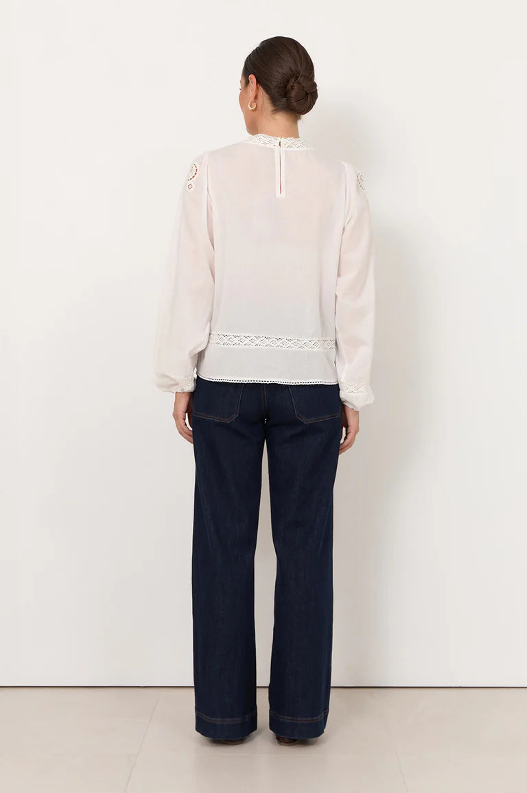 Woman wearing a Adorne white blouse with lace details and dark pants on a white background