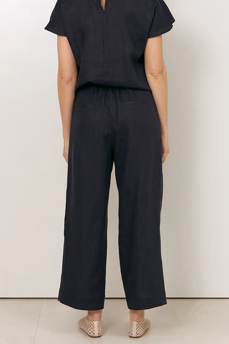 Image of A model shown from the back wearing a Adorne dark navy blue short-sleeve top and matching wide-leg cropped pants, paired with beige woven flat shoes, against a plain off-white wall.
