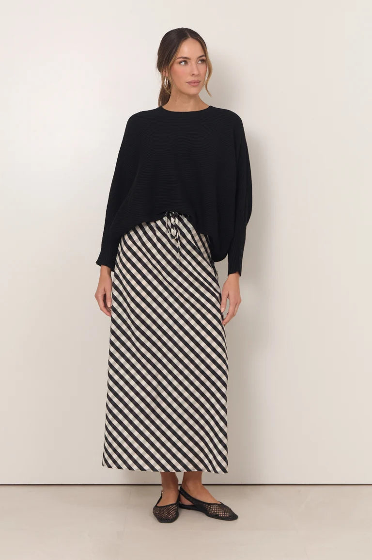 Image of Woman wearing a black sweater and Adorne black and white striped skirt against a white background