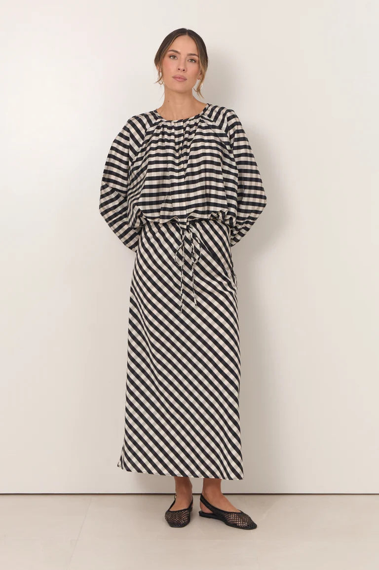 Image of A woman modeling a Adorne black and white striped midi dress with a tie waist and long balloon sleeves, standing against a plain off-white wall.