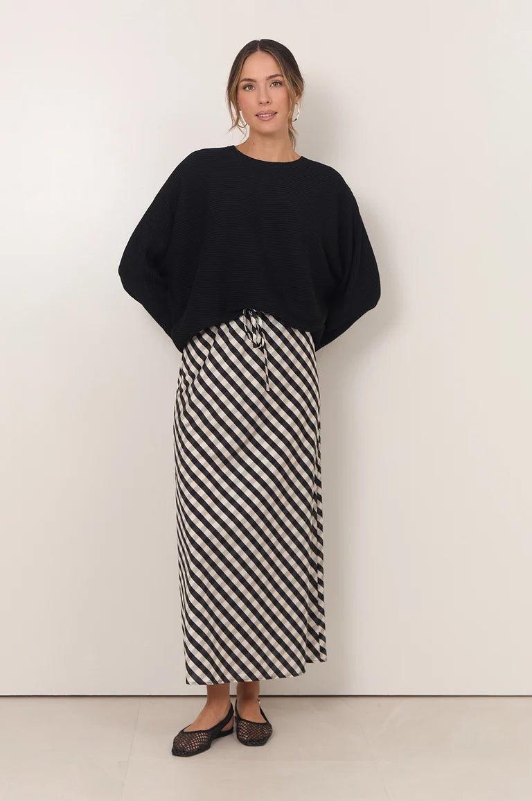 Image of A woman modeling a black long-sleeve top and a Adorne black and white diagonally striped midi skirt, standing against a plain off-white wall.