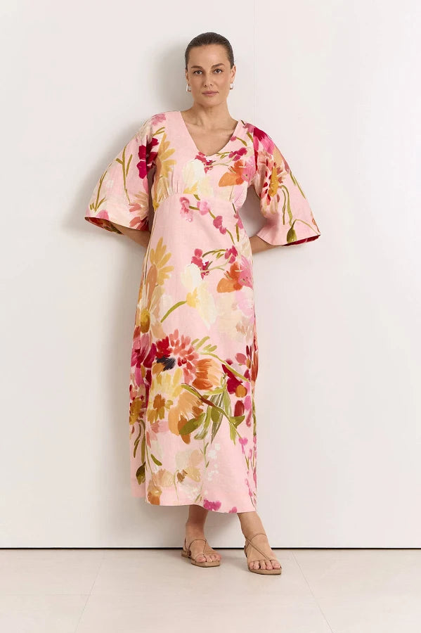 Image of A woman modeling a Adorne light pink kaftan dress with a vibrant multicolor floral print, standing against a plain white wall.
