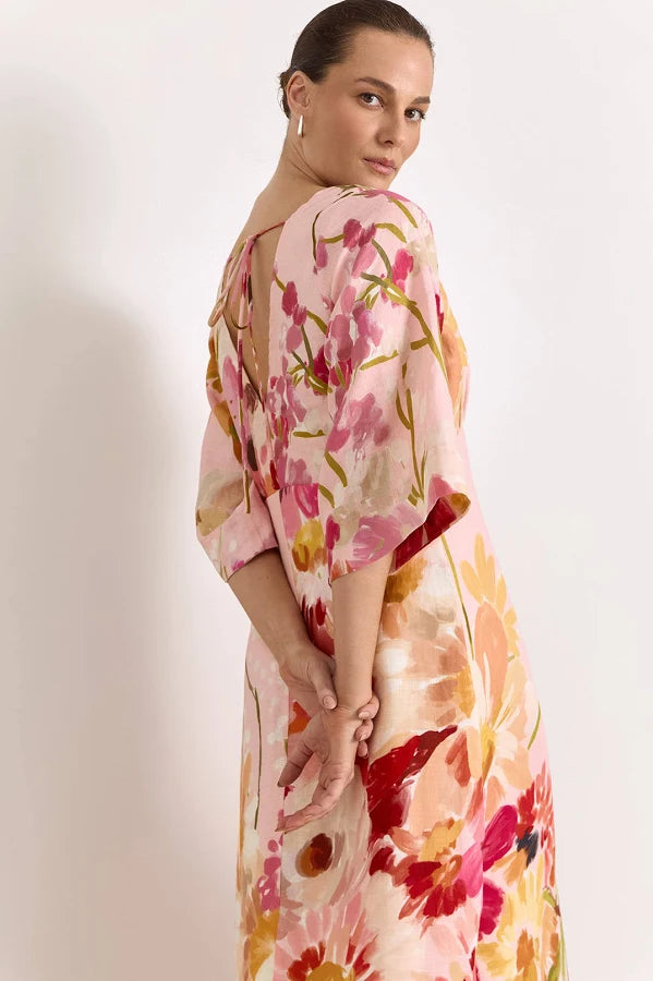 Image of A woman wearing a Adorne light pink floral dress with pink, red, and yellow watercolor-style flowers, photographed against a plain off-white studio background.