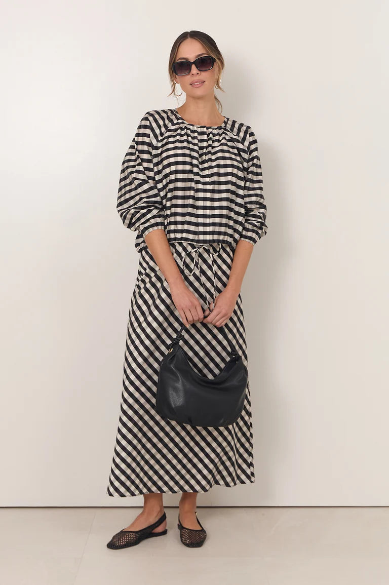 Woman wearing a Adorne black and white striped dress holding a black handbag against a white background
