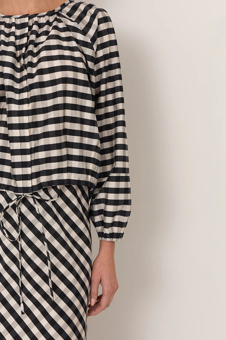 Image of A close-up of a woman wearing a Adorne black and off-white striped garment with a gathered neckline, long sleeves, and a drawstring waist, against a plain light wall.
