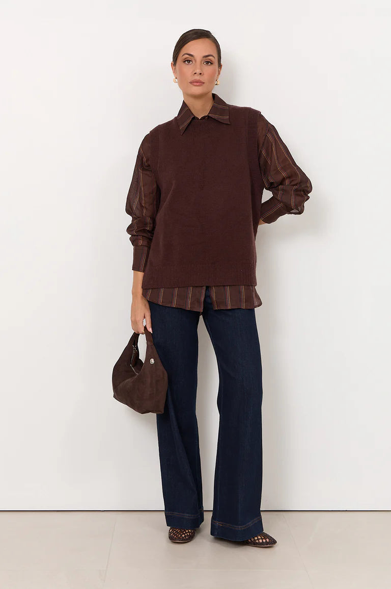 Image of Woman wearing a Adorne brown shirt and dark jeans, holding a brown handbag against a white background