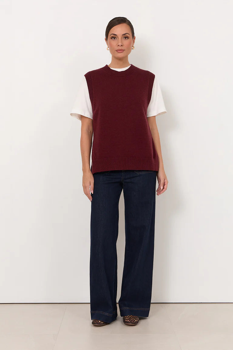 Woman wearing a Adorne burgundy sleeveless top and dark pants against a white background