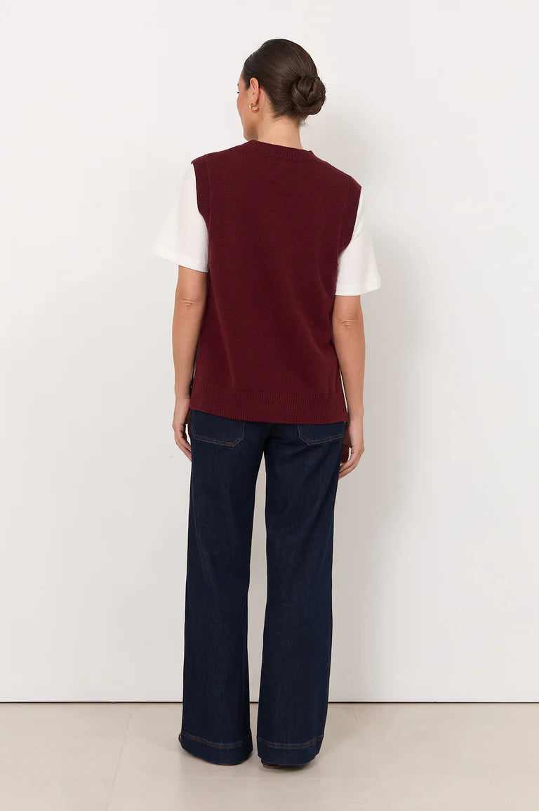Woman wearing a Adorne burgundy vest over a white shirt with dark blue pants on a white background