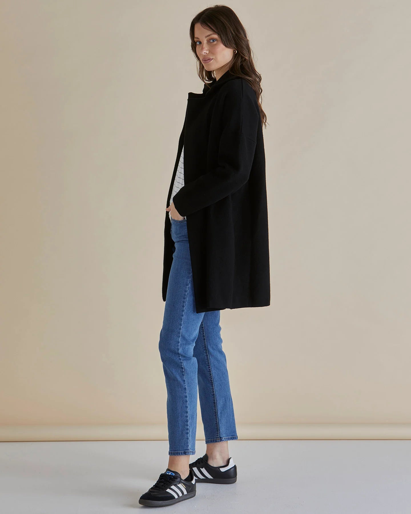 Image of Woman wearing a Betty Basics black coat and blue jeans standing against a beige background