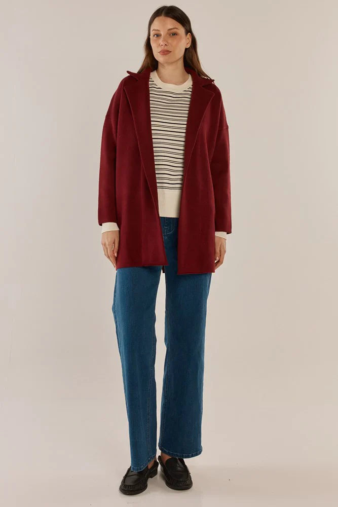 Image of Woman wearing a Betty Basics red coat, striped shirt, and blue jeans on a beige background