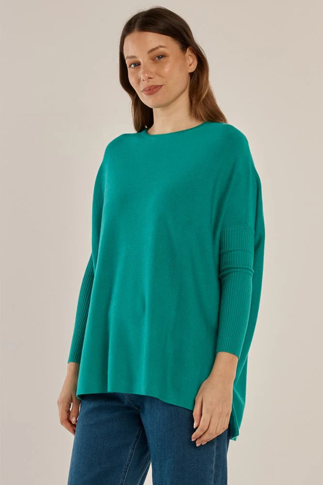 Woman wearing a Betty Basics teal sweater and blue jeans against a beige background