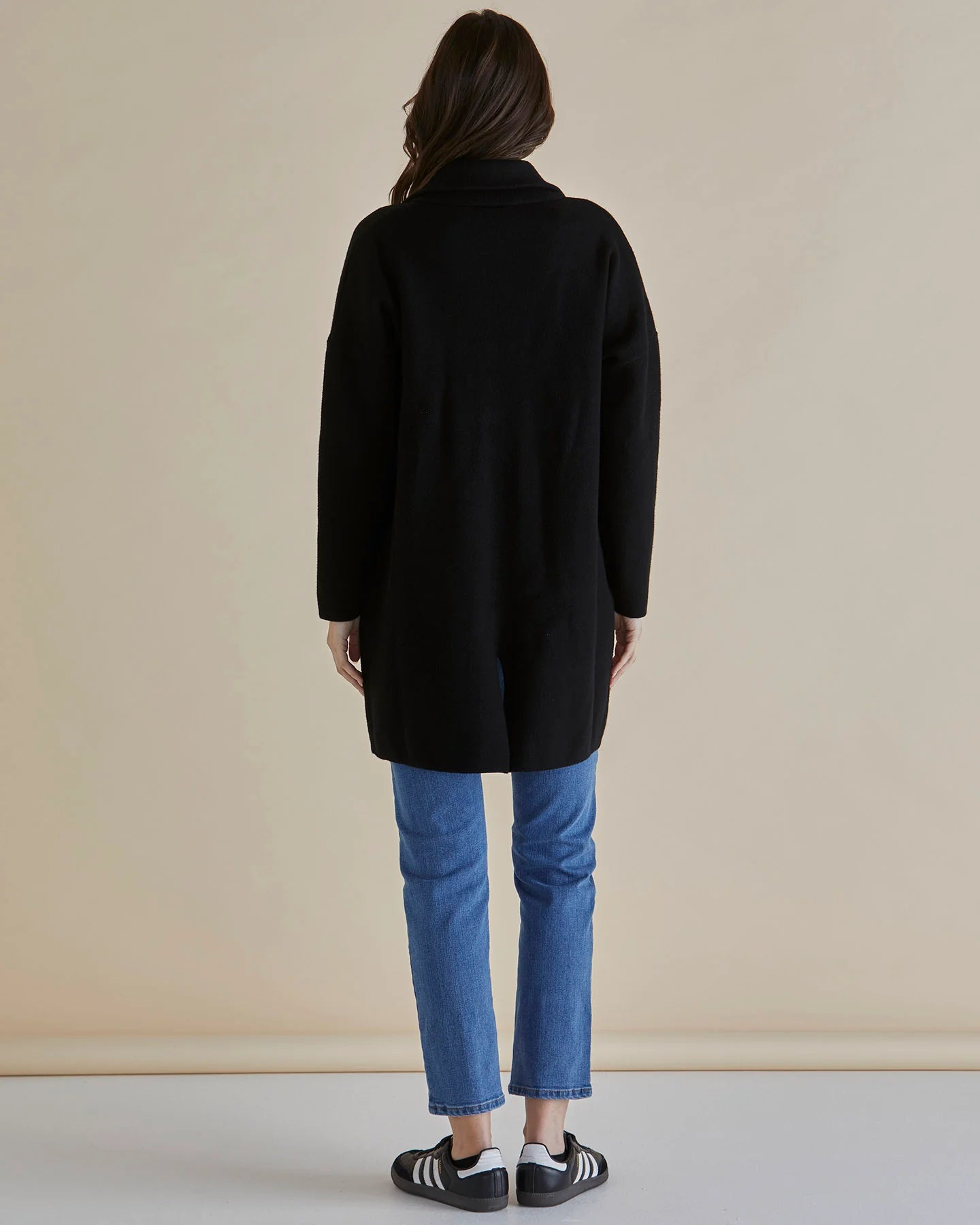 Woman wearing a Betty Basics black coat, gray striped shirt, and blue jeans against a beige background