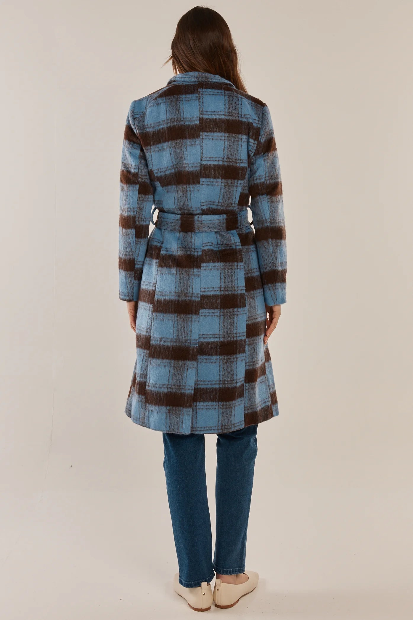Woman wearing a Betty Basics blue and brown plaid coat on a plain background