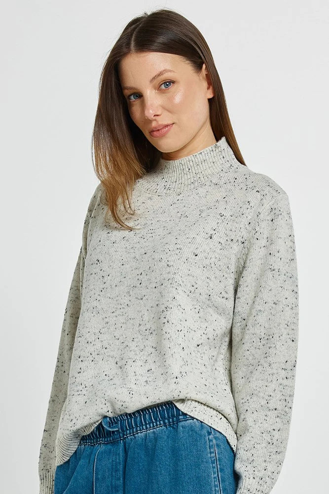 Woman wearing a Betty Basics gray speckled sweater and blue jeans on a white background