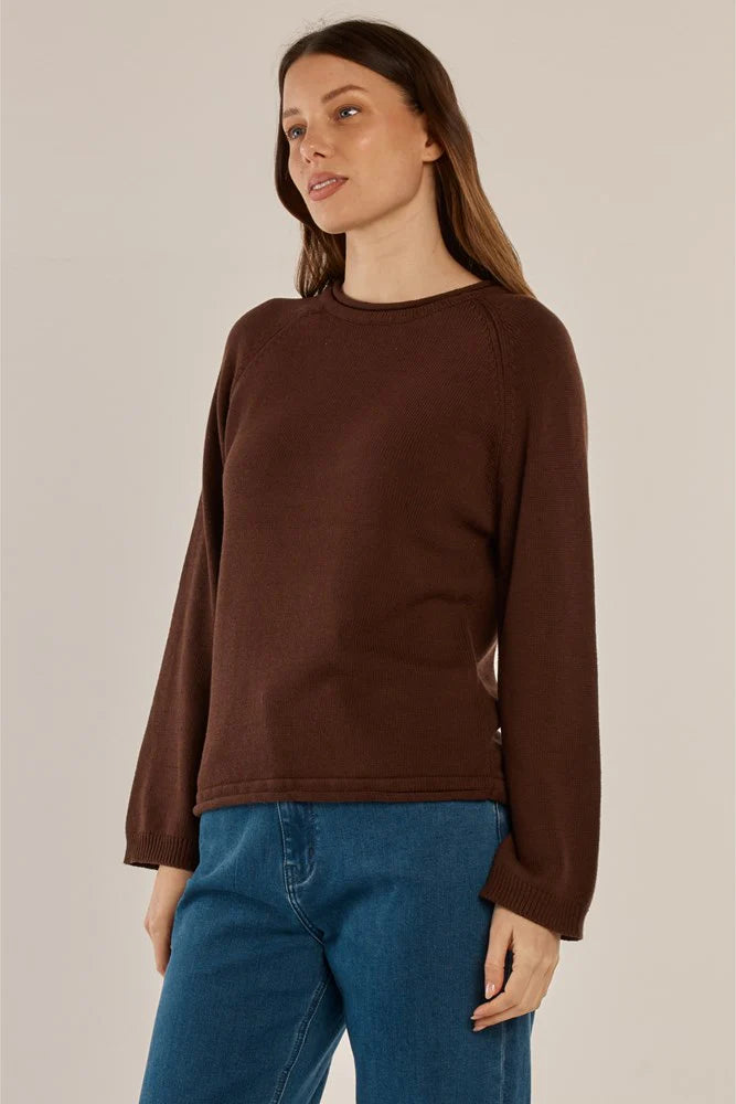 Woman wearing a Betty Basics brown long-sleeve top and blue jeans on a beige background