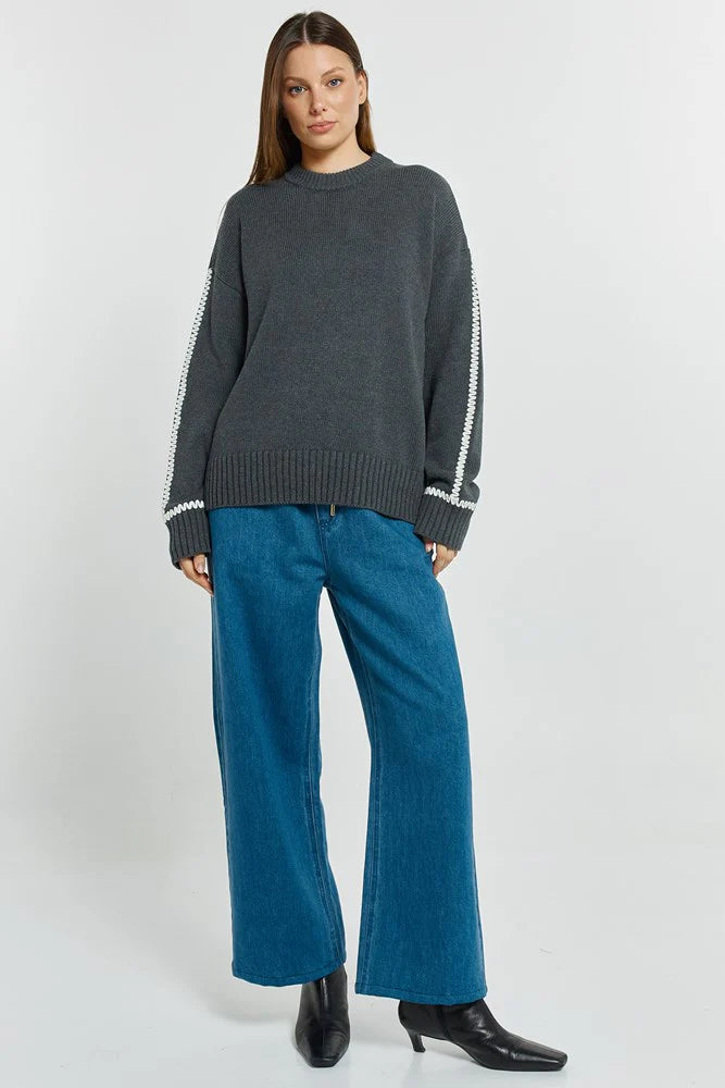 Image of Woman wearing a Betty Basics dark gray sweater with white trim and blue jeans on a white background