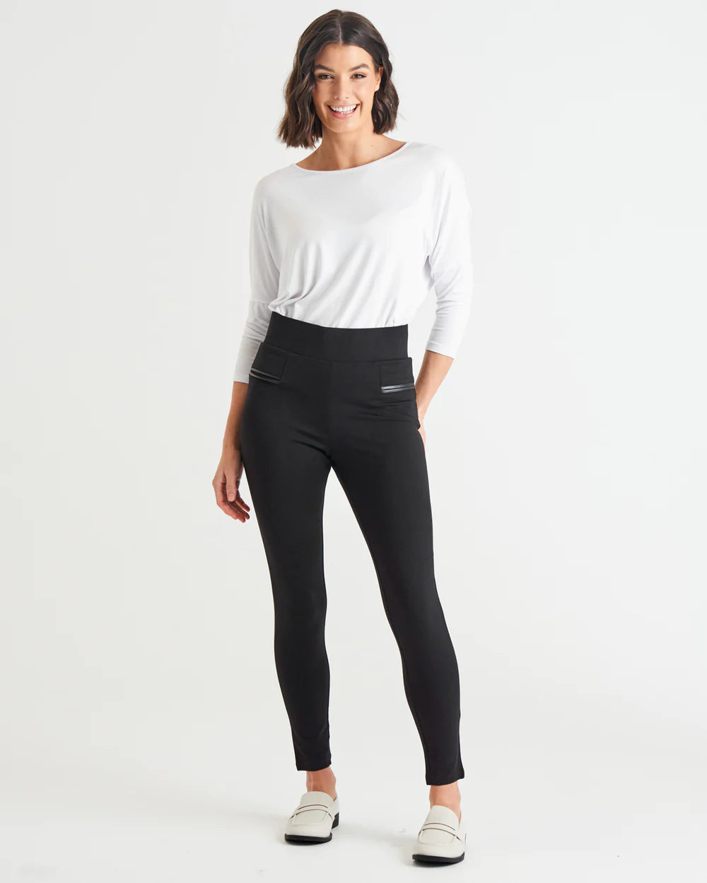 A model wearing mid-high rise Betty Basic black ponte leggings with a flat front waist and skinny leg design, paired with a white top.