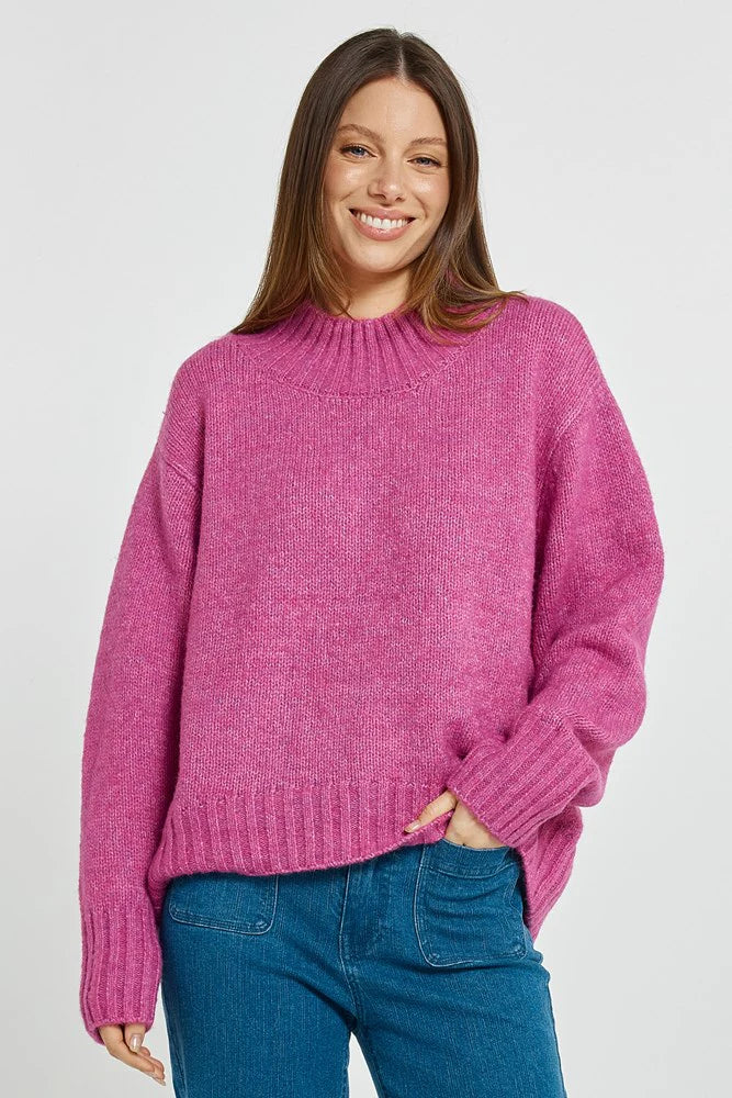 Woman wearing a Betty Basics pink sweater and blue jeans on a white background