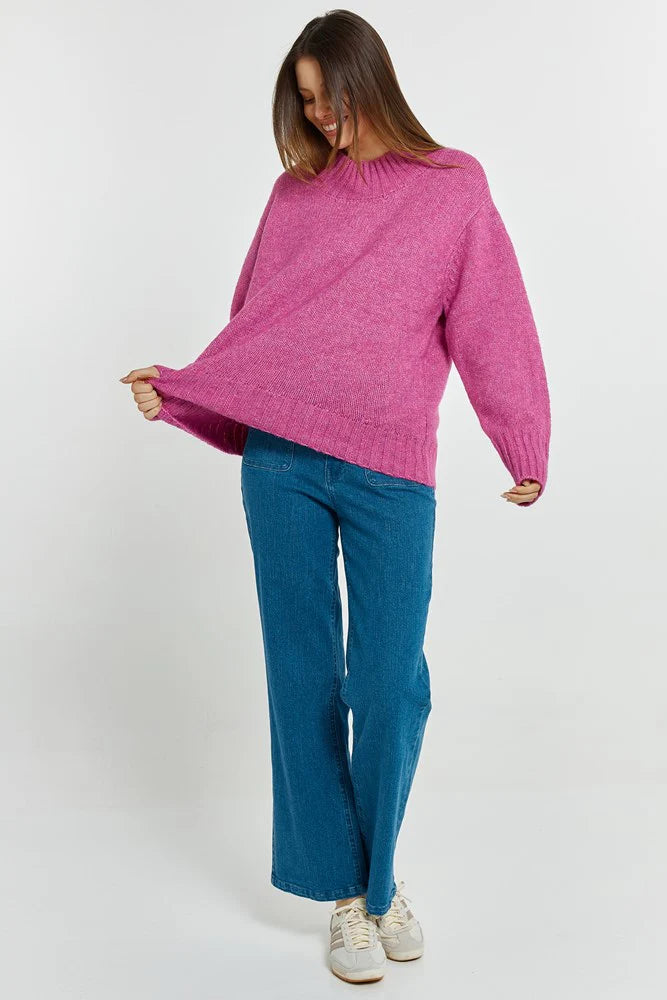 Woman wearing a Betty Basics pink sweater and blue pants on a white background