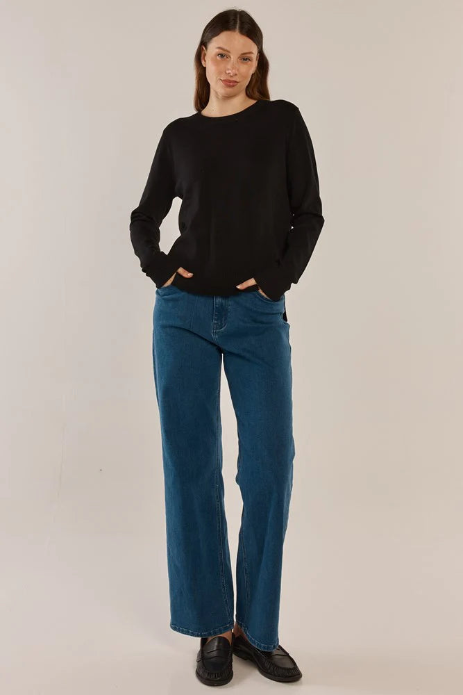 Woman wearing a Betty Basics black sweater and blue jeans against a plain background