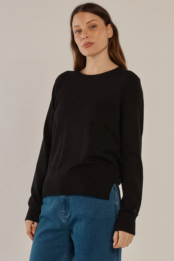 Woman wearing a Betty Basics black sweater and blue jeans against a plain background