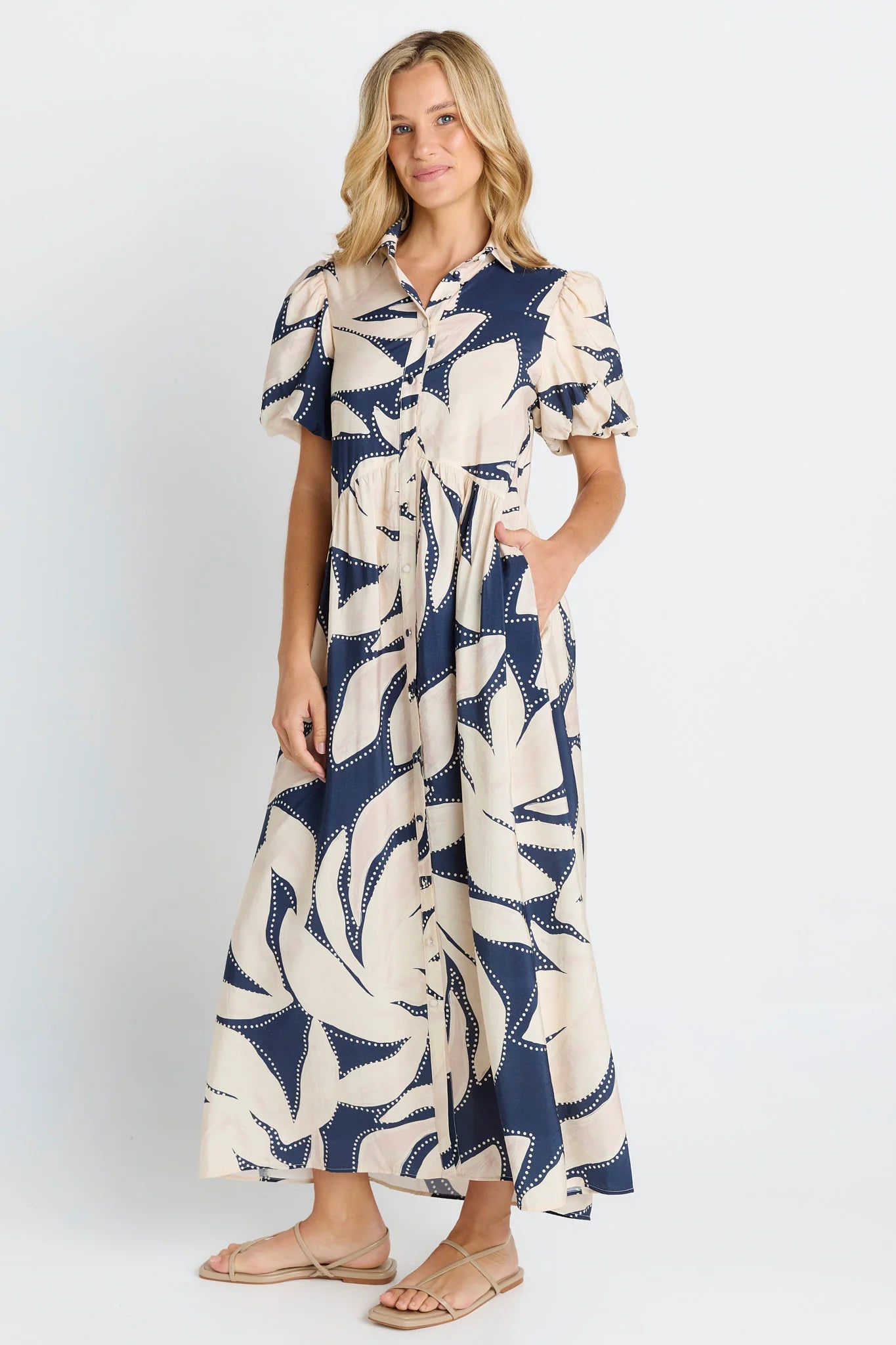 Image of A woman modeling a Betty Basics short-sleeve midi dress with a navy blue and cream abstract botanical pattern, standing against a light gray studio background.