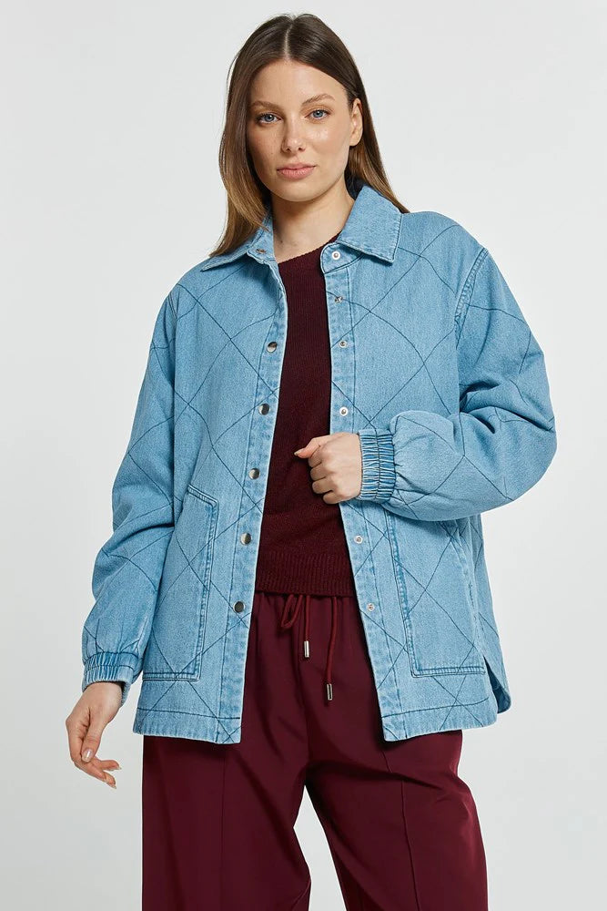 Woman wearing a Betty Basics blue quilted jacket over a maroon top and pants on a white background
