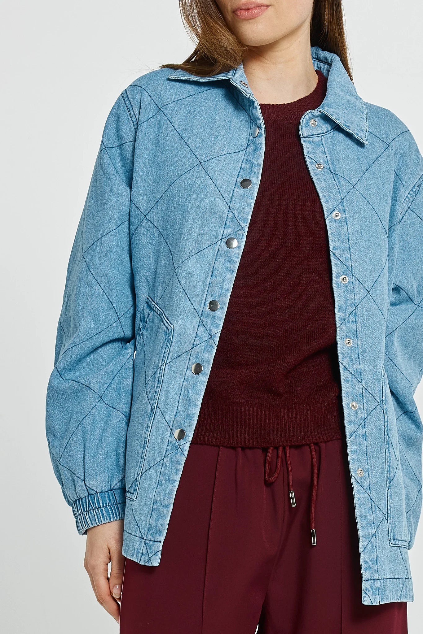 Woman wearing a Betty Basics light blue denim jacket over a dark red sweater and pants on a white background