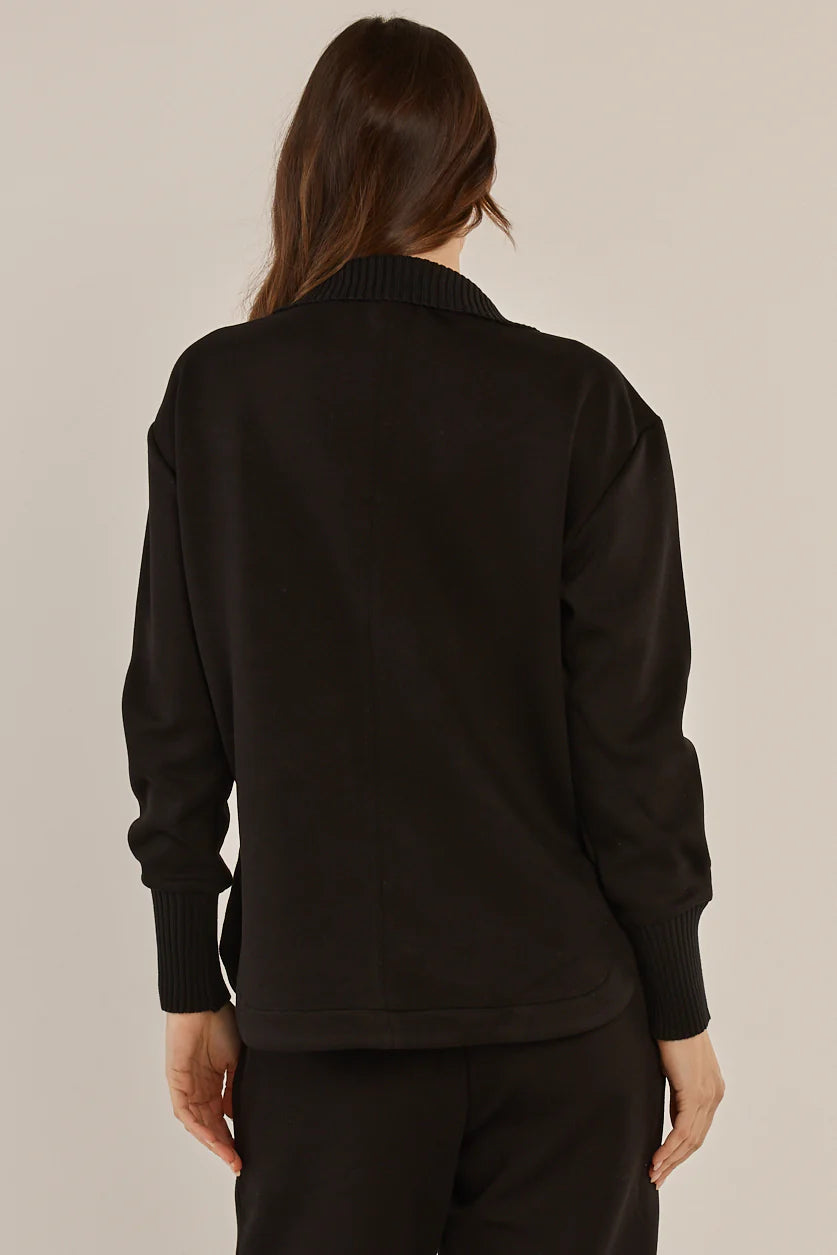 Image of Woman wearing a Betty Basics black sweater and pants on a beige background