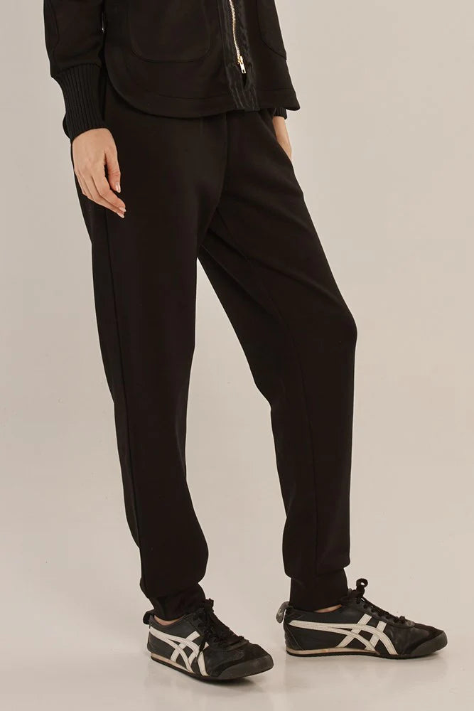 Woman wearing Betty Basics black pants and black sneakers on a plain background