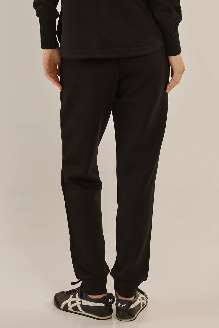 Woman wearing Betty Basics black pants and black and white sneakers on a plain background
