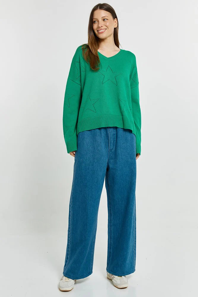 Image of Woman wearing a Betty Basics green sweater and blue jeans on a white background