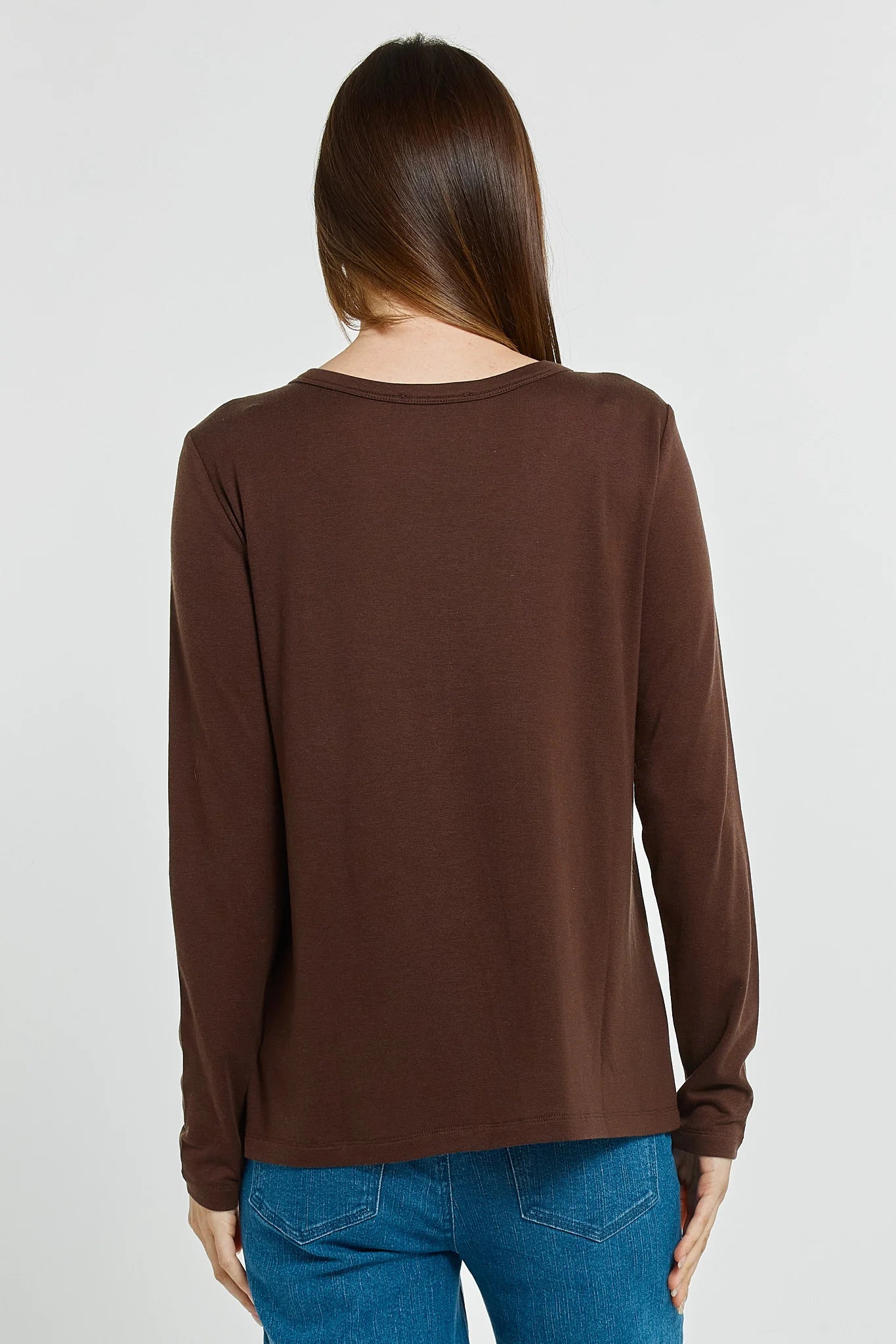 Woman wearing a Betty Basics brown long-sleeve top and blue jeans on a white background
