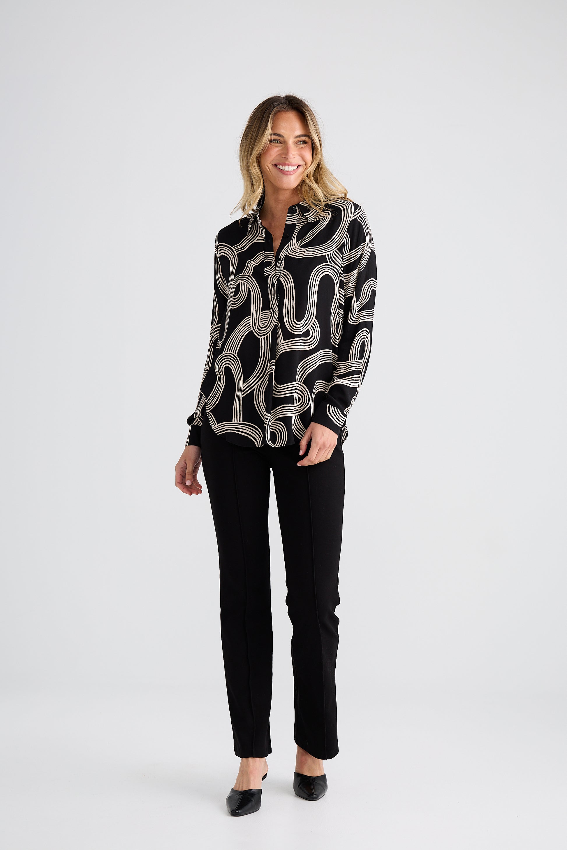 Woman wearing a Brave and True black and white patterned blouse with black pants on a white background