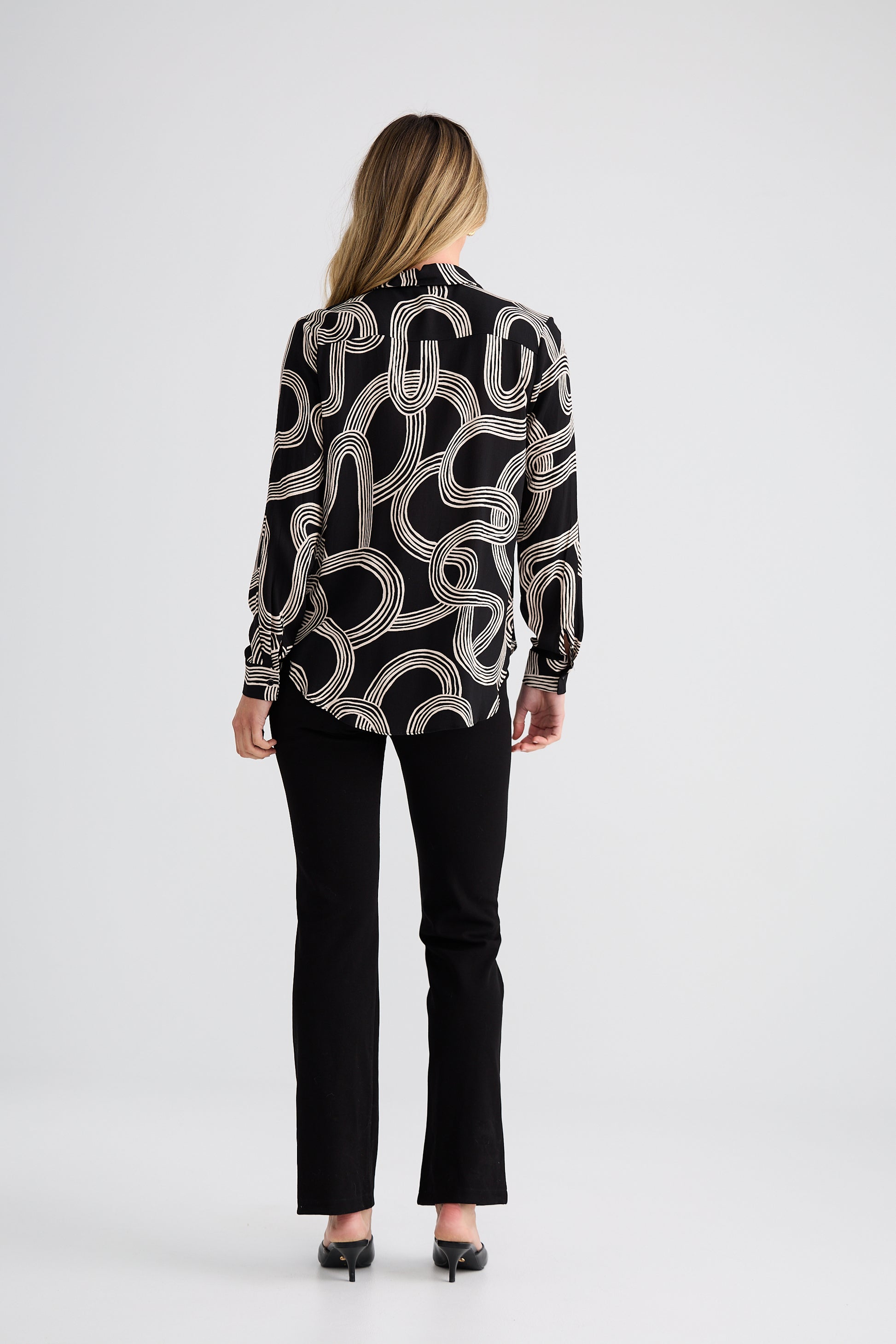 Woman wearing a Brave and True black and white patterned blouse with black pants on a white background