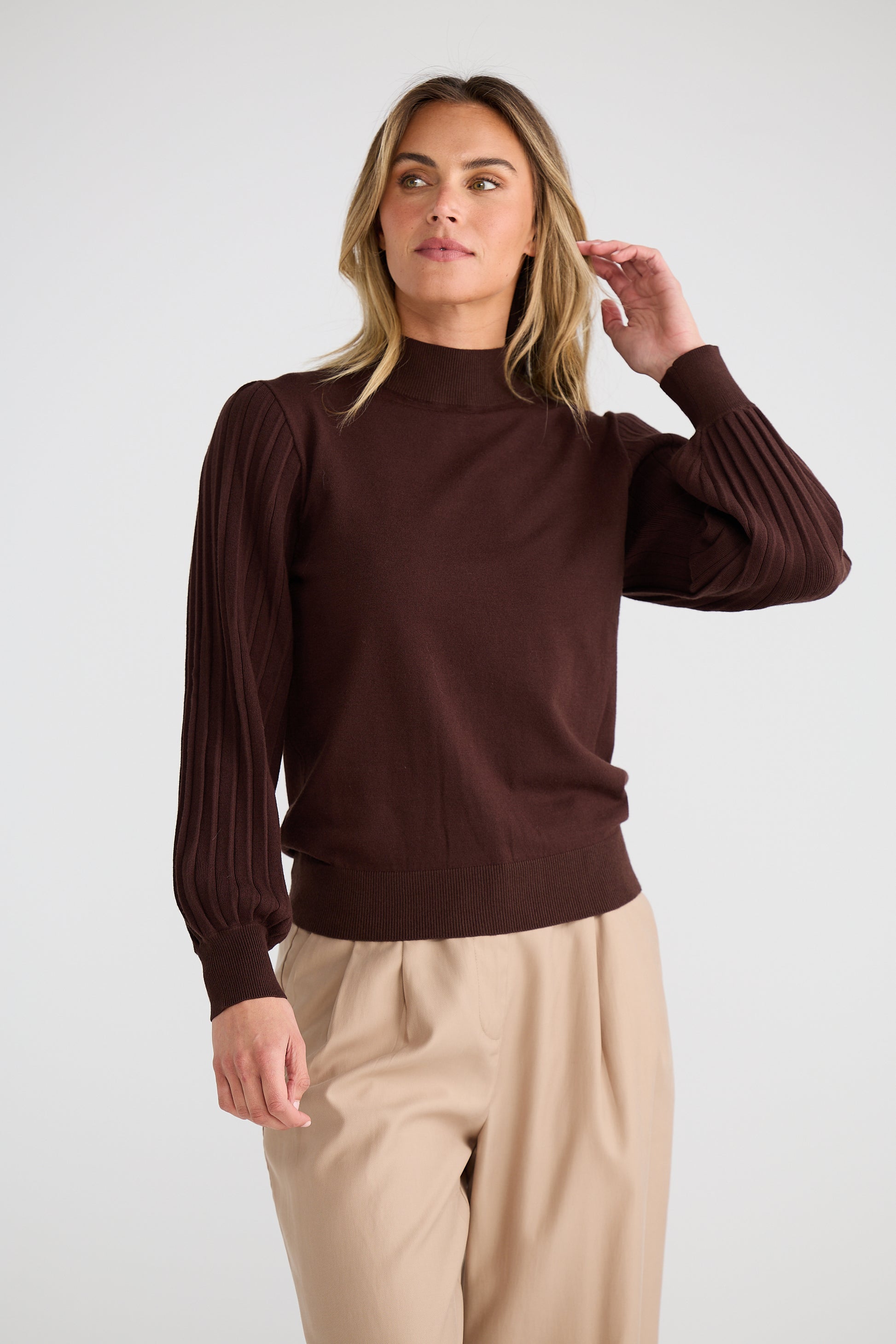 Woman wearing a Brave and True brown sweater and beige pants against a white background