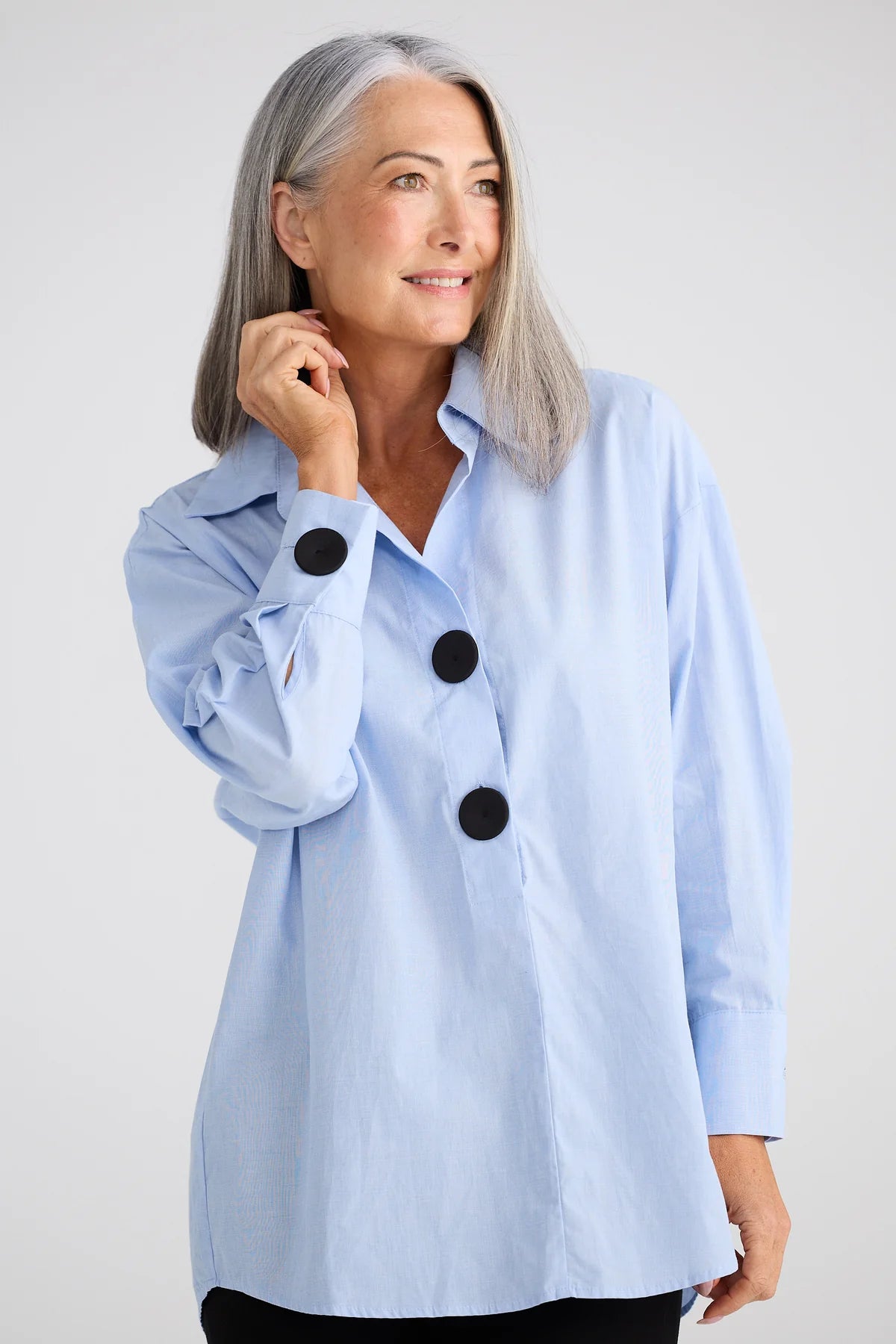 Image of Woman wearing a Brave and True light blue shirt with black buttons against a white background