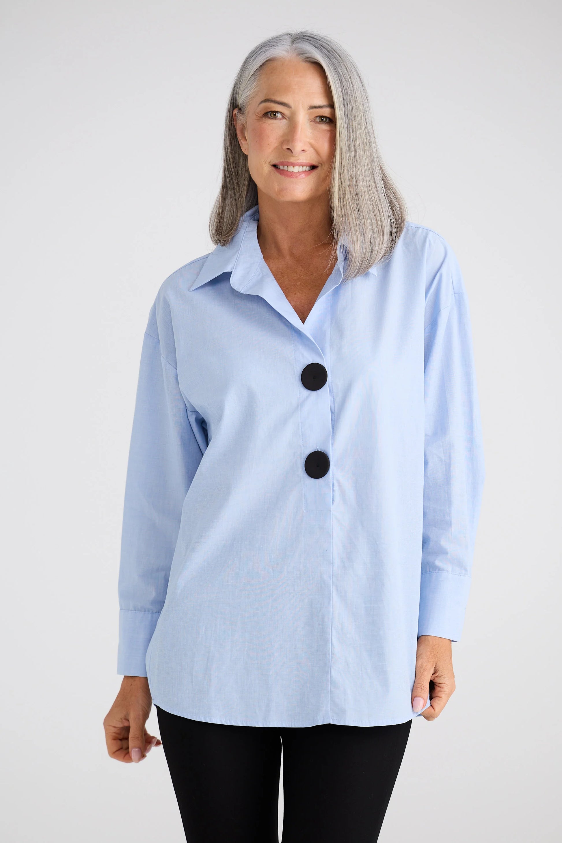 Woman wearing a Brave and True light blue button-up shirt with black buttons on a white background