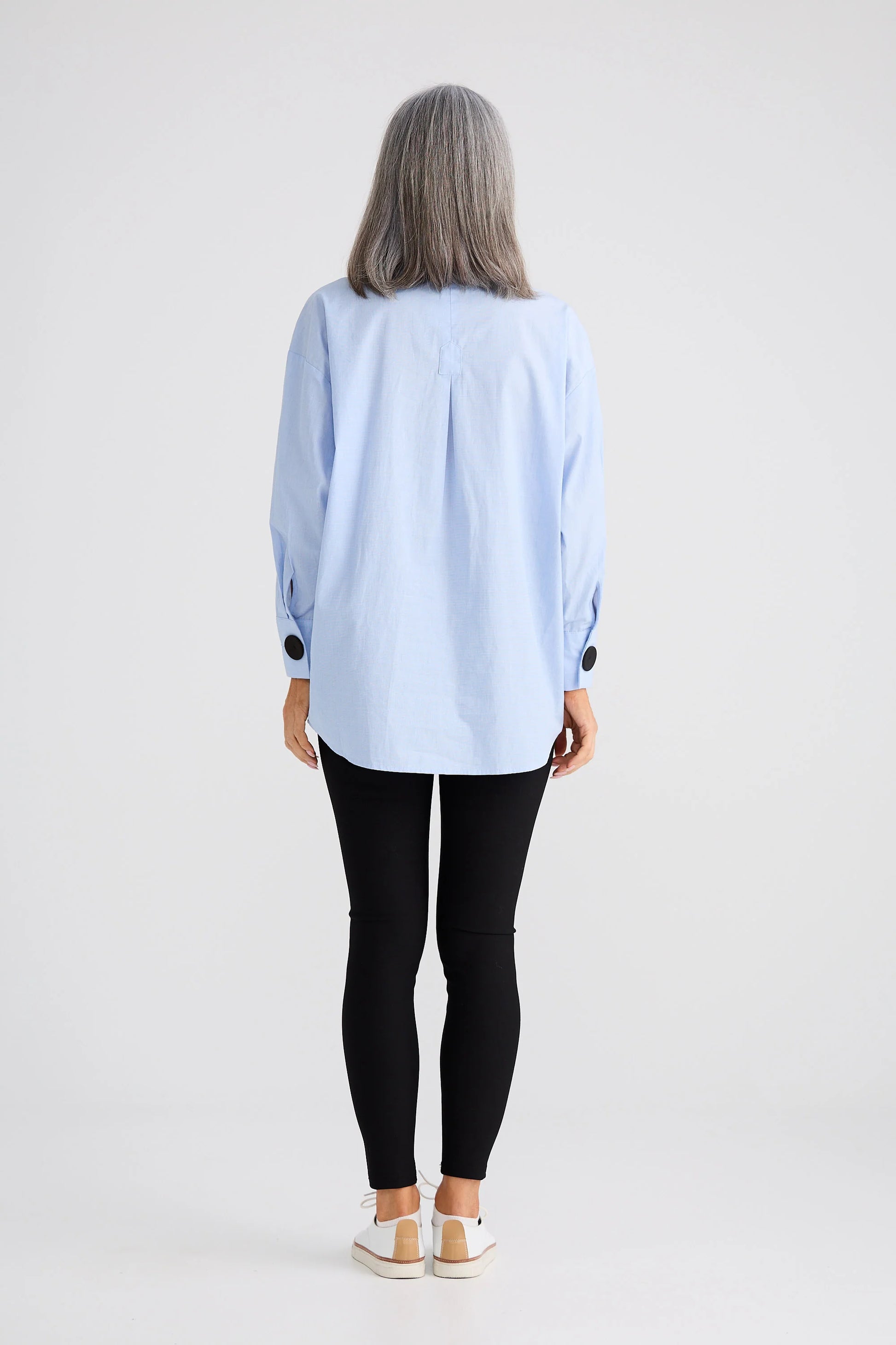 Woman wearing a Brave and True light blue shirt and black pants on a white background