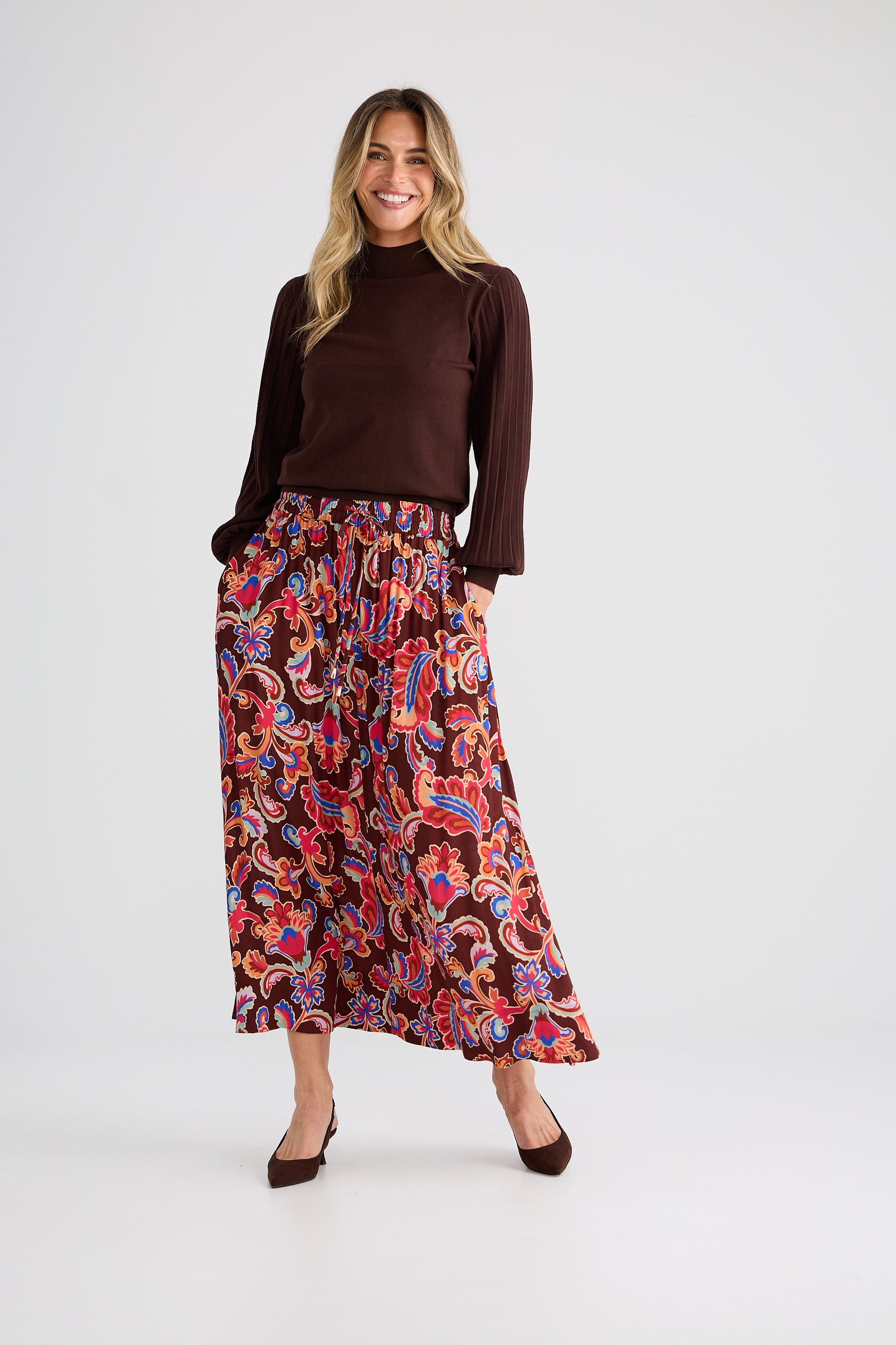 Woman wearing a brown top and Brave and True colorful patterned skirt on a white background
